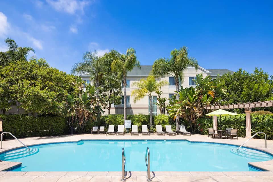 Resort pool surrounded by palm trees and lounge chairs with white umbrella on sunny day