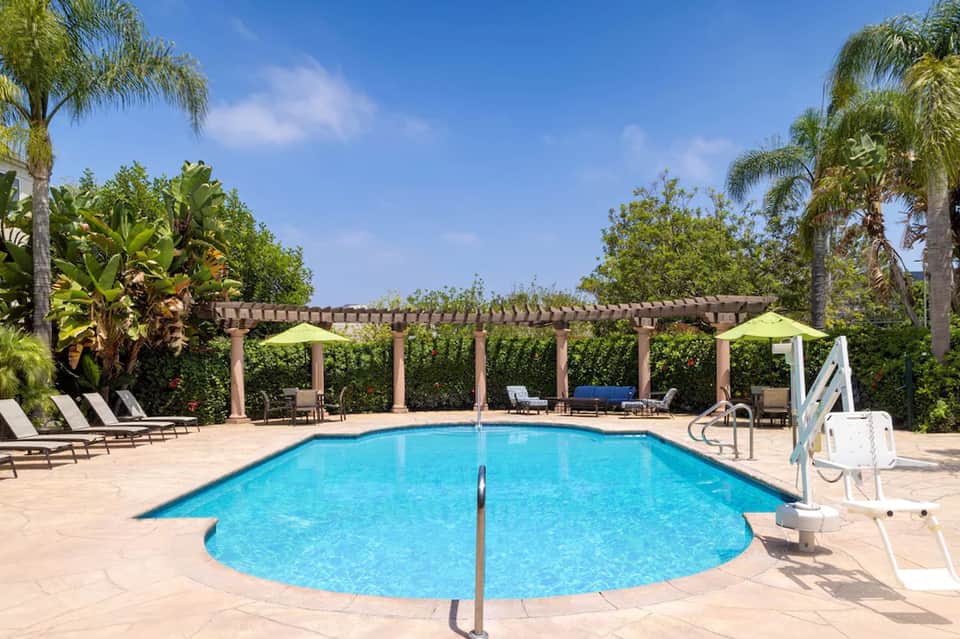 Resort swimming pool with lounge chairs and wooden pergola structure surrounded by palm trees