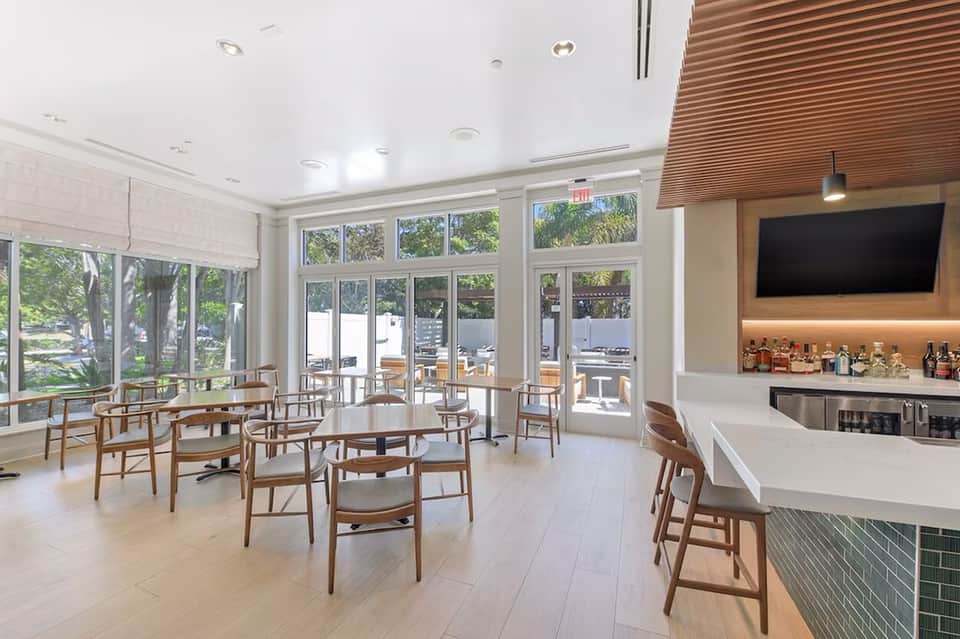 Bright cafe space with wooden chairs, white bar counter, large windows, and outdoor seating visible