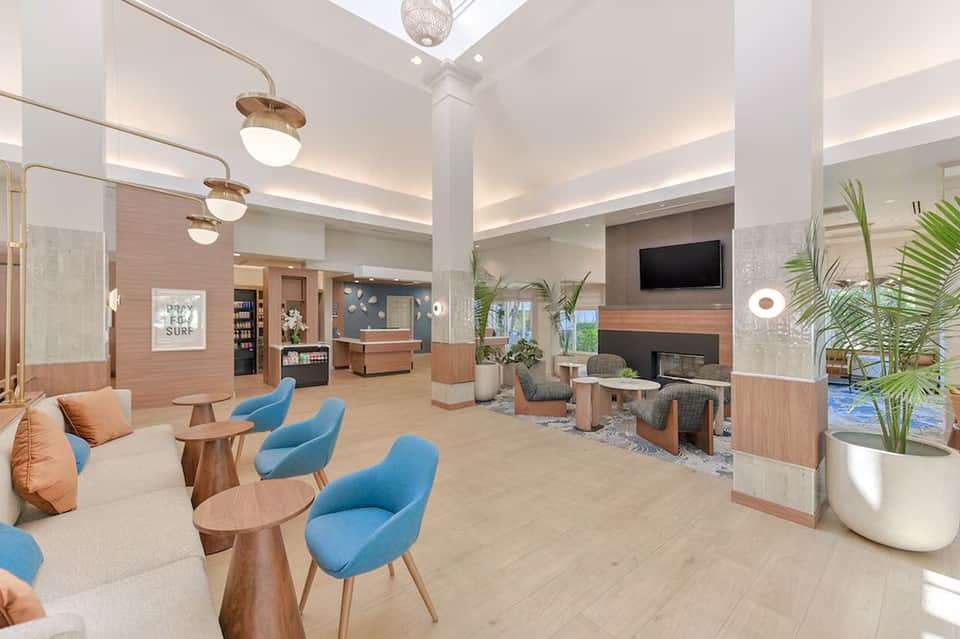 Modern hotel lobby with wooden accents, blue chairs, fireplace, and contemporary lighting