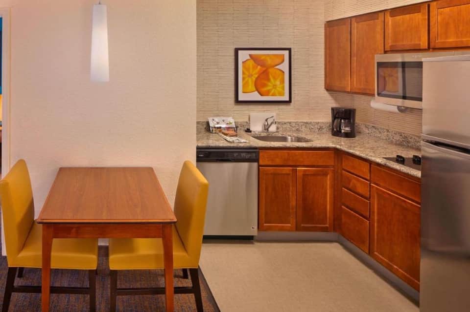 Hotel suite kitchenette with wood cabinets, granite counters, and yellow dining chairs