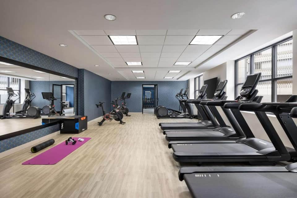 Spacious fitness center with treadmills, exercise bikes, blue accent walls, and large windows