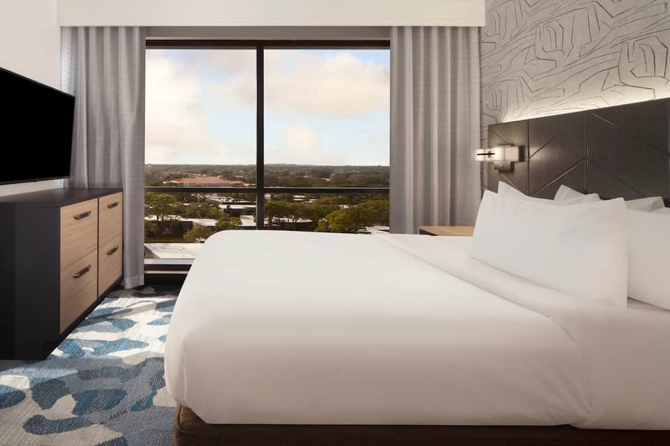Modern hotel bedroom with king bed, panoramic windows overlooking landscape, and contemporary furnishings