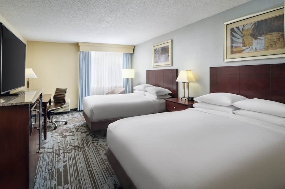 Hotel guest room with two queen beds, dark headboards, and desk area