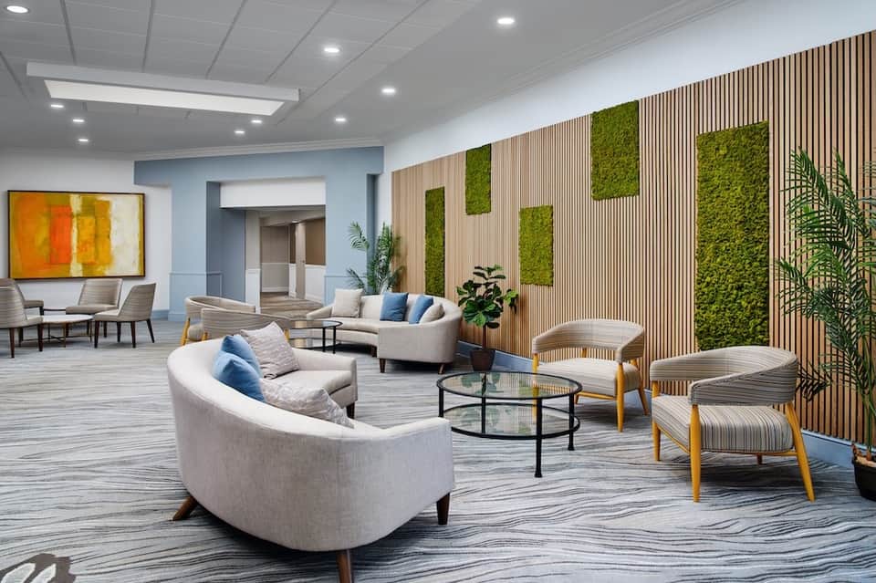 Modern hotel lobby lounge with curved seating, green plant walls, wood paneling, and contemporary furniture