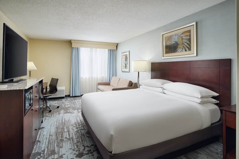 Hotel room with king bed, desk, TV, and sitting area with modern furnishings