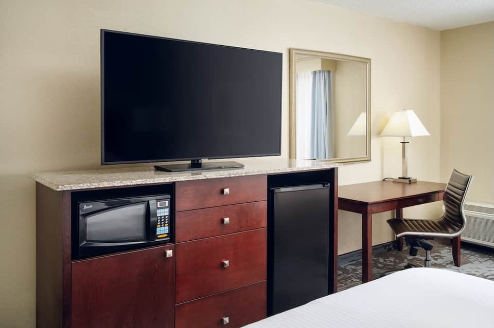 Hotel room with TV, desk, microwave, and mirror reflecting the bedroom area