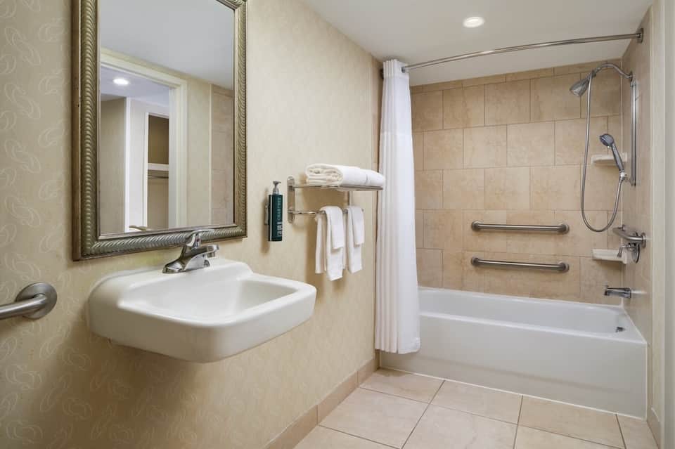 Clean bathroom with white sink, framed mirror, beige tile walls, white shower curtain, and accessible grab bars