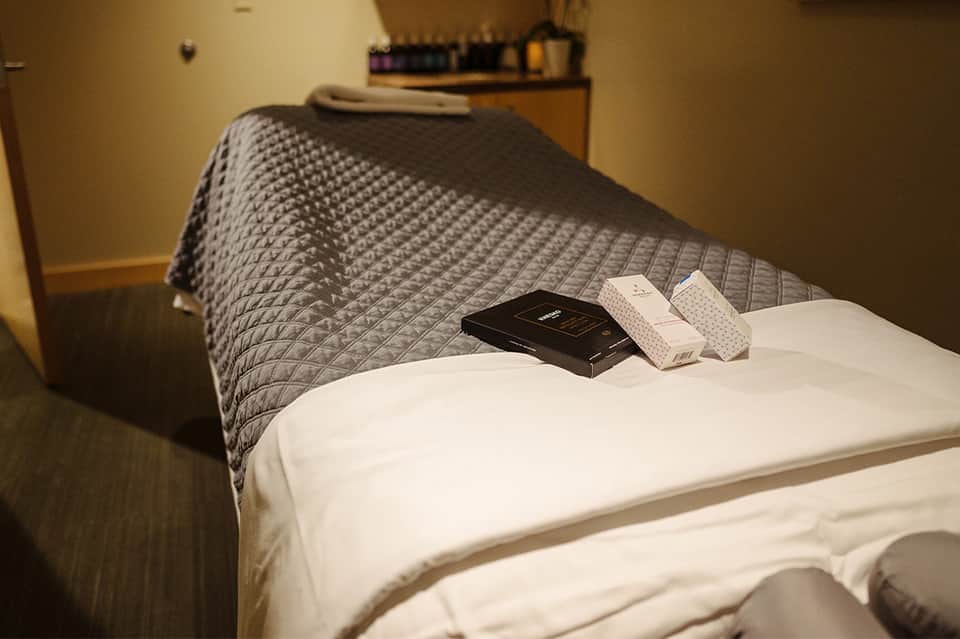 Spa treatment bed with folded towel and amenities on white bedding