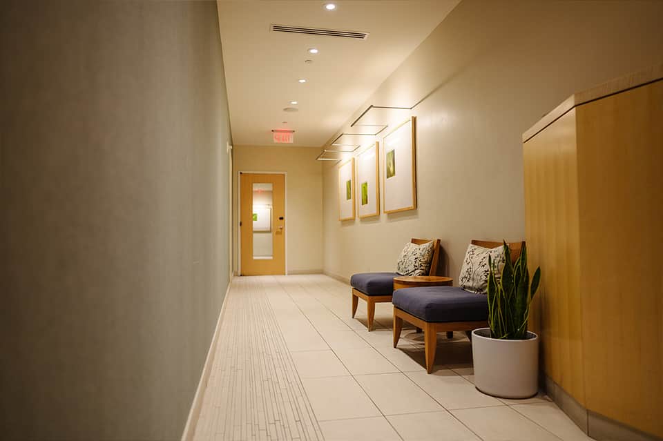 Contemporary hallway with light wood accents, blue cushioned seating, and recessed lighting