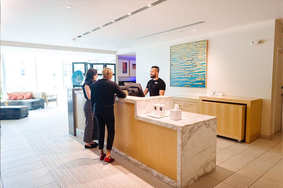 Modern hotel lobby with marble reception desk, staff assisting guests, and contemporary decor