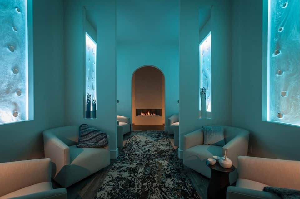 Spa relaxation room with turquoise walls, glowing accent lighting, and fireplace centerpiece