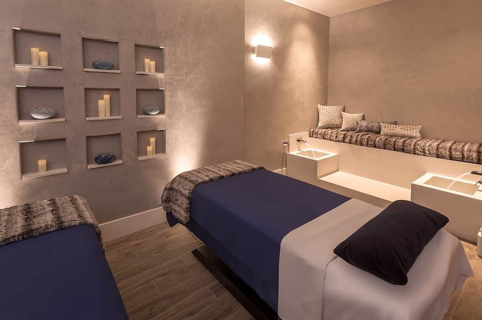 Spa treatment room with massage beds, decorative wall niches with candles and shells, neutral tones