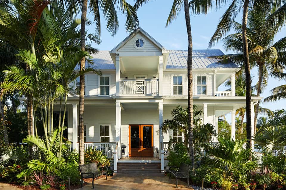 Elegant white two-story home with columns, metal roof, and palm tree landscaping