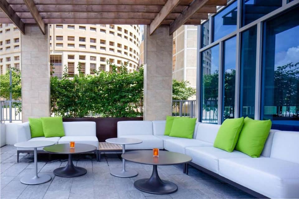 Rooftop lounge with white seating, green accent pillows, and urban cityscape views