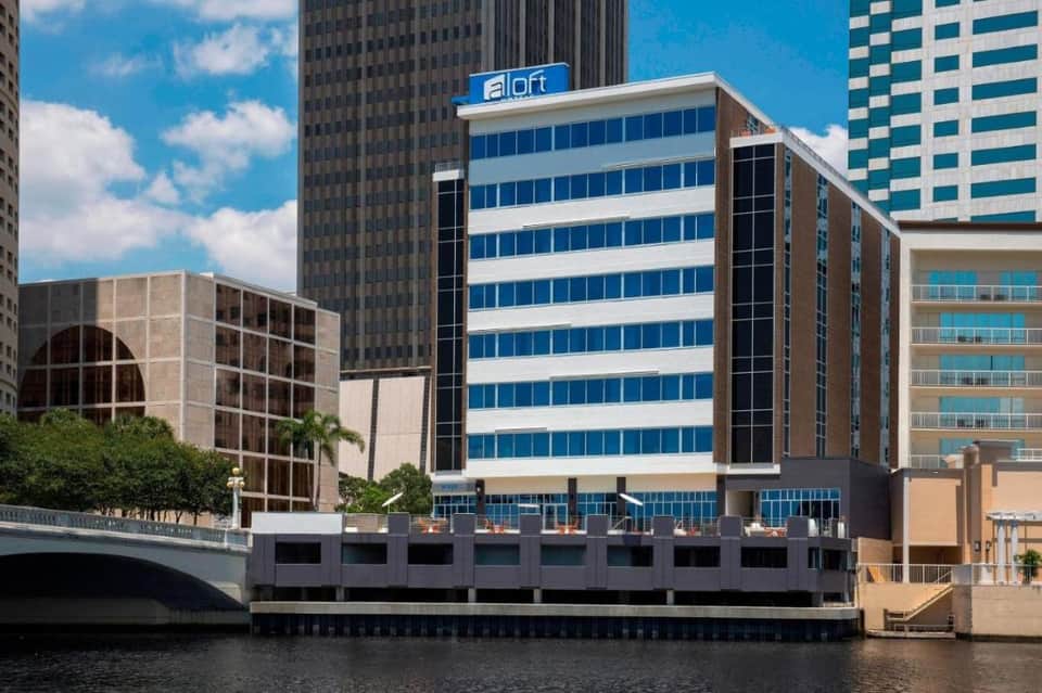 Aloft hotel waterfront building with blue and white striped facade along river with bridge and downtown skyline