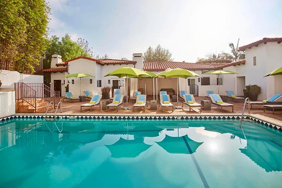 Resort pool with turquoise water, lounge chairs under lime green umbrellas, and Spanish architecture