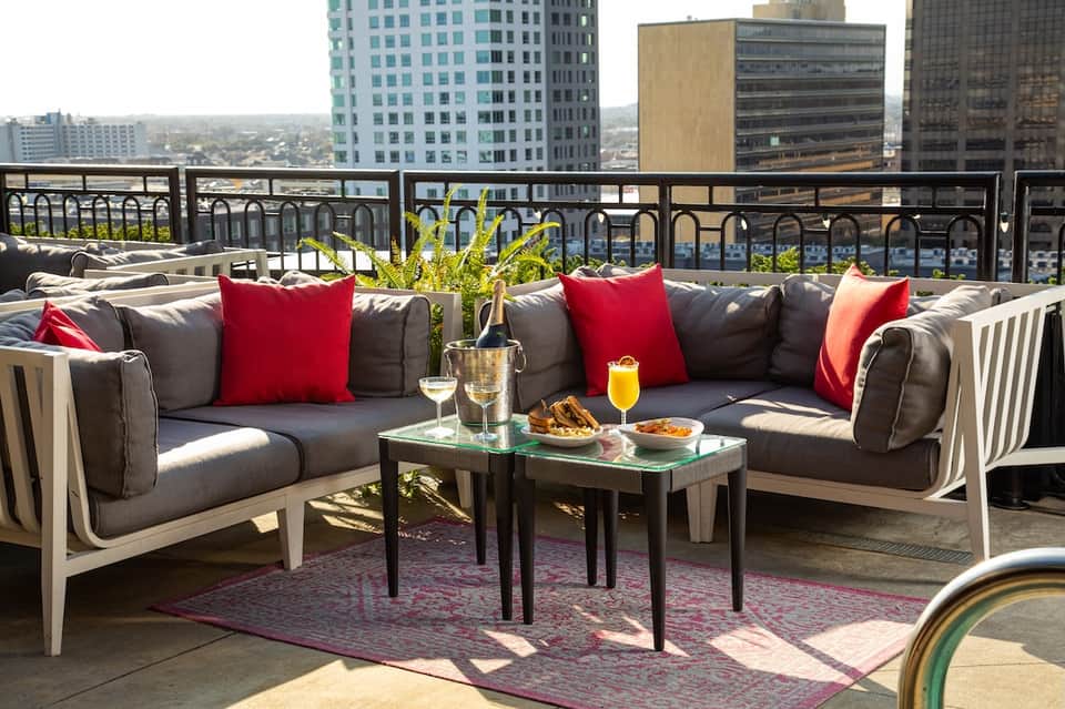 Modern rooftop lounge with gray sectional sofa, red pillows, and cityscape view