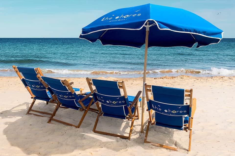 Beach umbrellas and loungers with 'The Shores' branding overlooking ocean waves