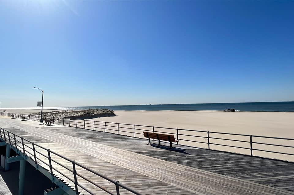Wooden boardwalk and empty sandy beach with calm ocean water and clear sky