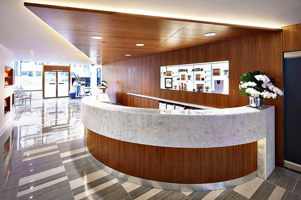 Modern medical or wellness reception desk with curved white marble counter and wood paneling