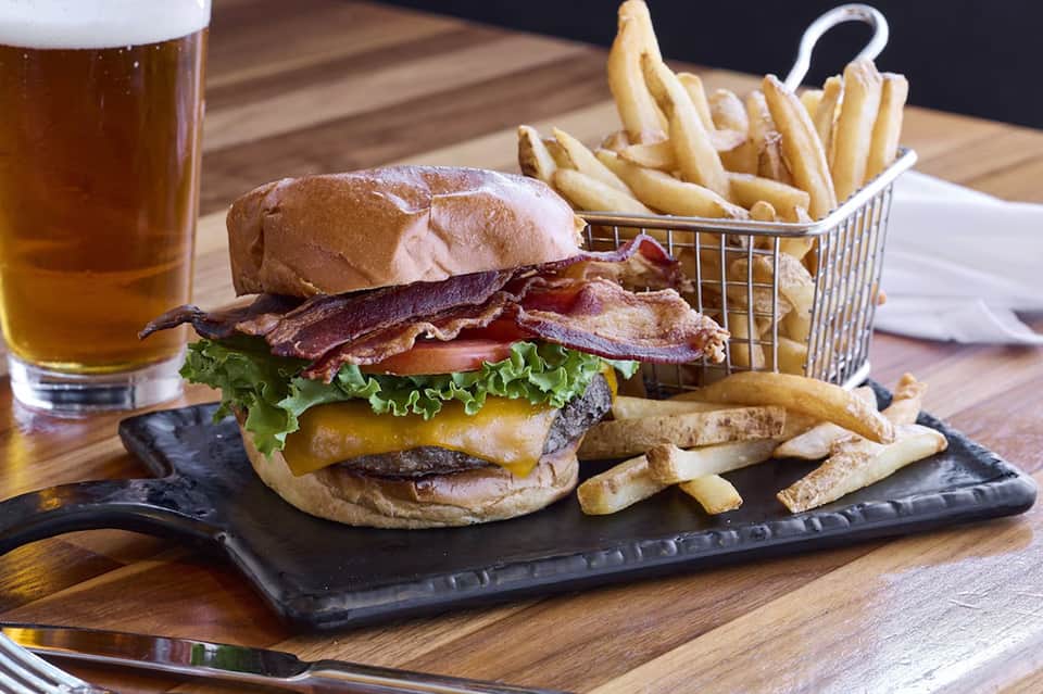 Gourmet burger with bacon and cheese served with fries and beer on wooden table