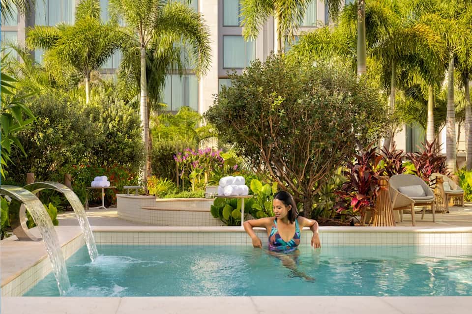 Woman enjoying tropical resort pool with palm trees, loungers, and modern building backdrop