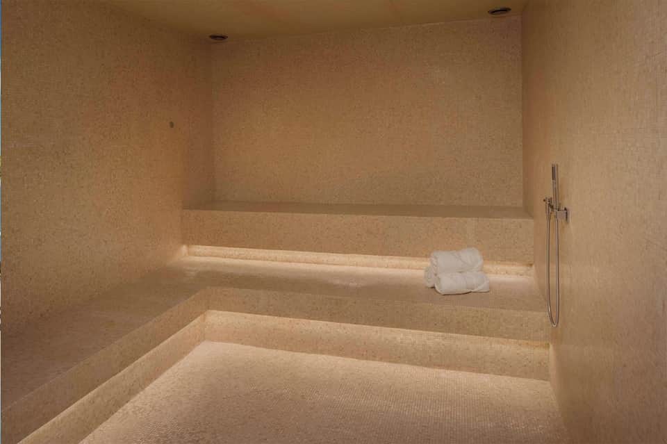 Luxurious spa steam room with golden tile walls, stepped seating, and ambient lighting