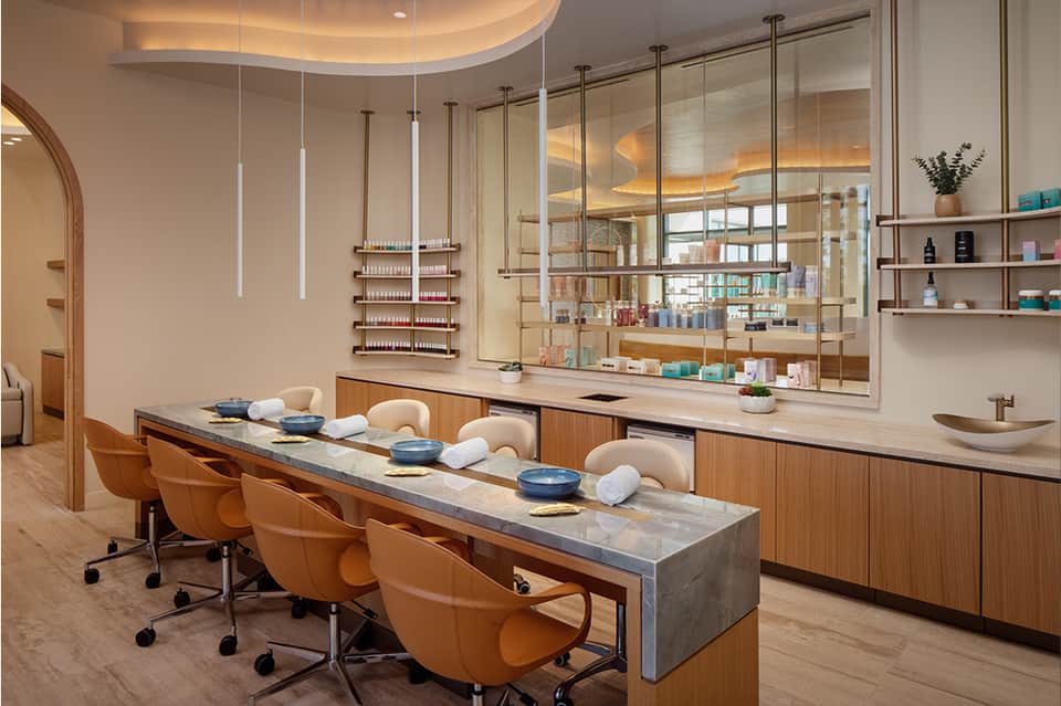 Modern salon interior with wooden counter, orange chairs, pendant lighting, and product display shelving