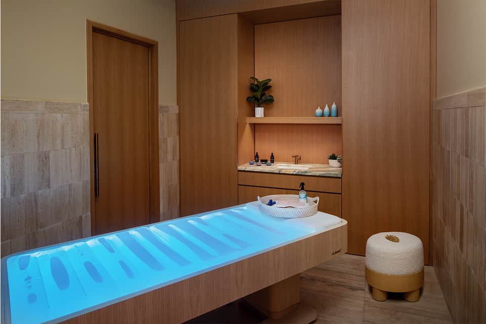 Spa bathroom with glowing blue soaking tub, wooden accents, and marble vanity