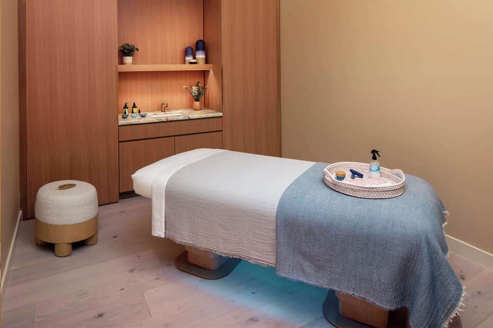 Spa treatment room with massage table, wooden accents, and amenity shelves