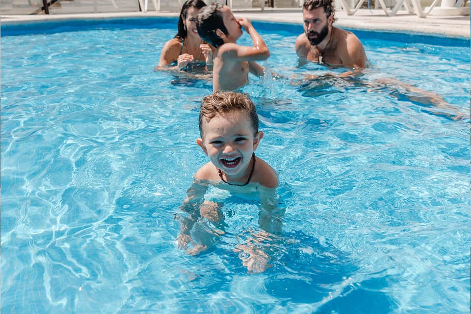 Family enjoying a bright blue swimming pool with a smiling young child in the foreground
