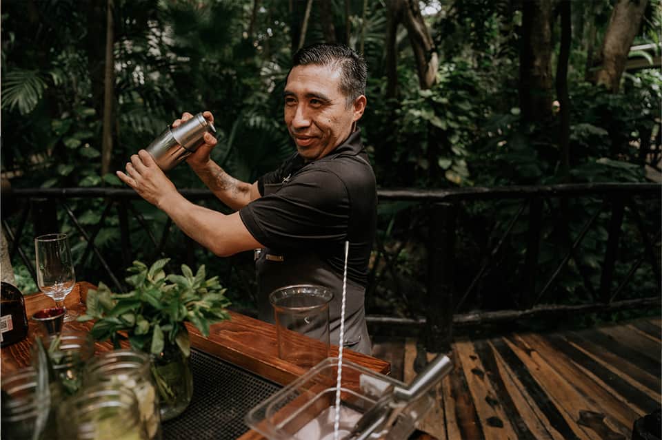 Bartender preparing cocktails outdoors surrounded by tropical jungle vegetation