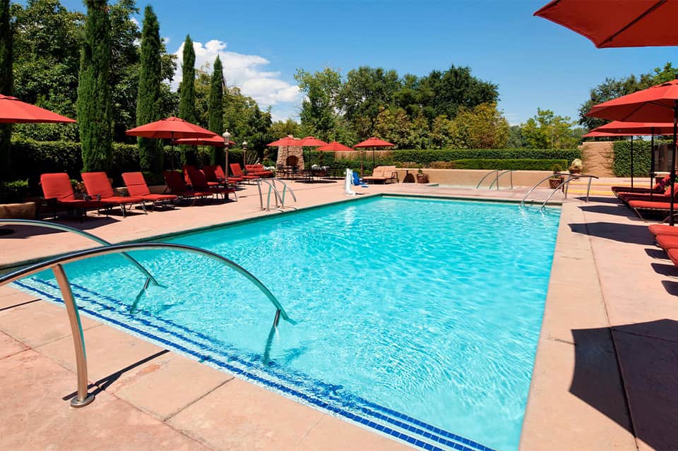 Resort pool with red umbrellas, red loungers, trees, and sunny day
