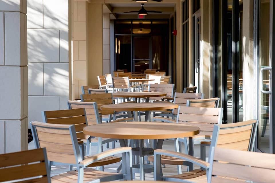 Outdoor patio dining area with wooden tables and blue-trimmed chairs under pergola