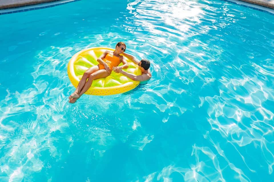 Two children playing on a yellow inflatable float in a bright turquoise swimming pool