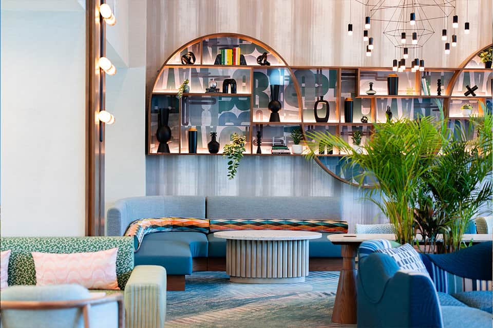 Modern hotel lobby with curved shelving, blue seating, decorative objects, and hanging lights