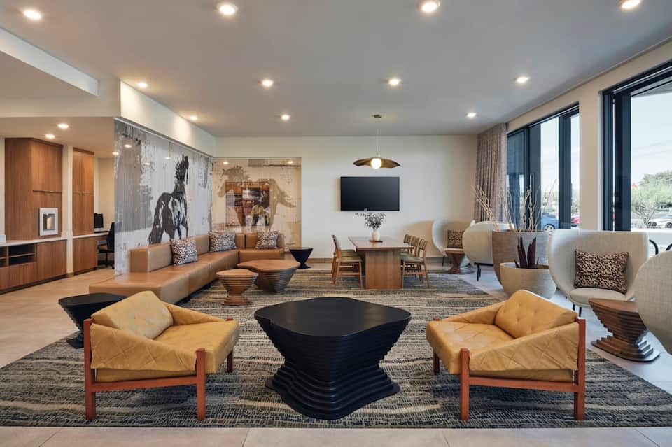 Contemporary hotel lobby with seating areas, TV, artwork, and large windows