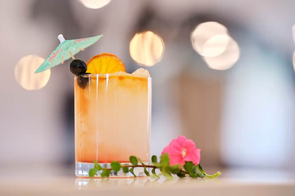 Tropical cocktail with umbrella garnish and flower decoration on blurred resort background