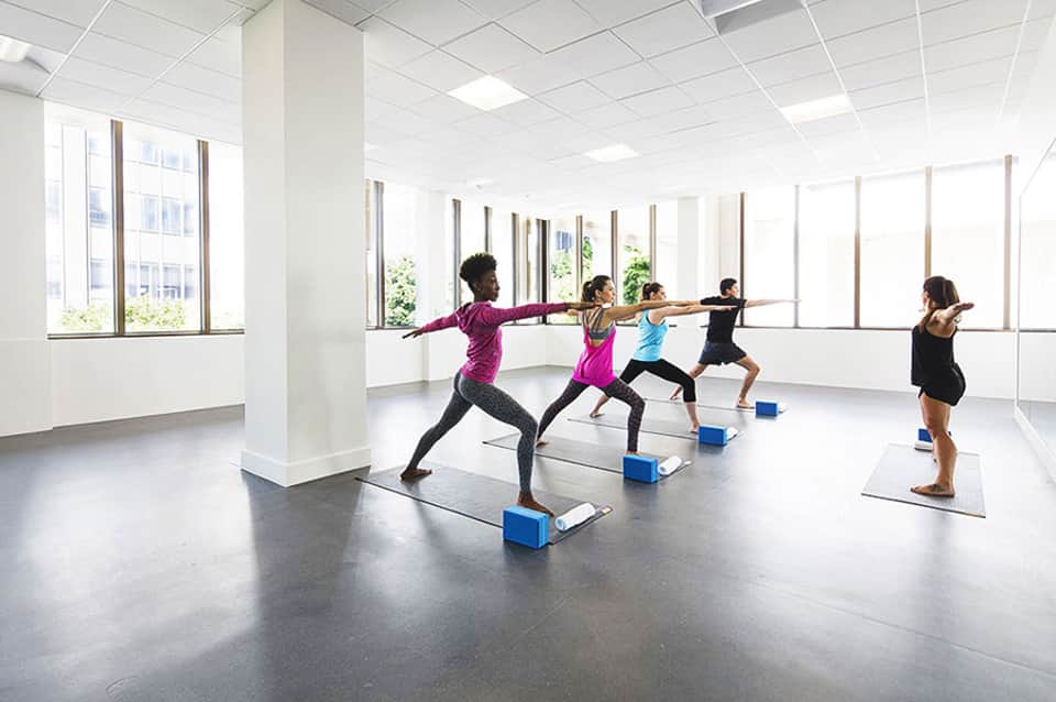 Fitness studio with five women performing yoga poses on mats with blue blocks during group class