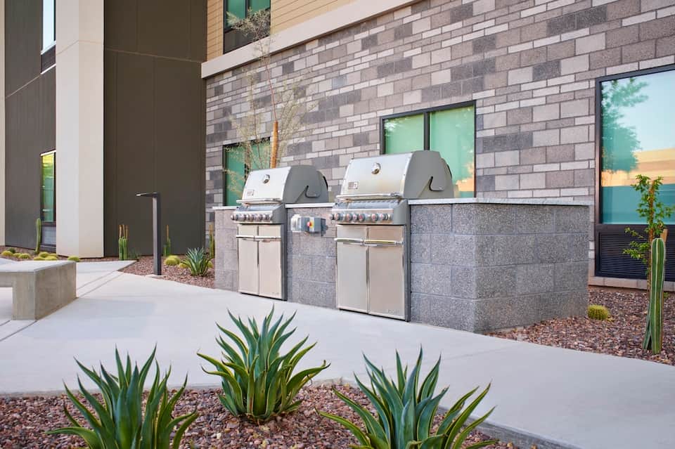 Two stainless steel built-in grills on patio with gray brick wall and desert landscaping
