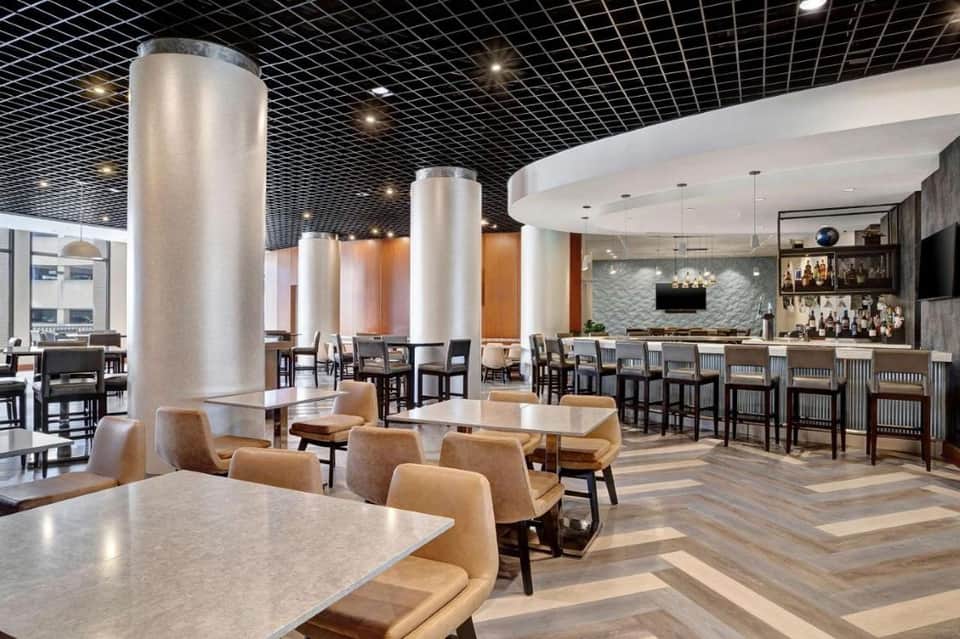 Contemporary hotel bar and lounge with metallic columns, wooden accents, full-service bar