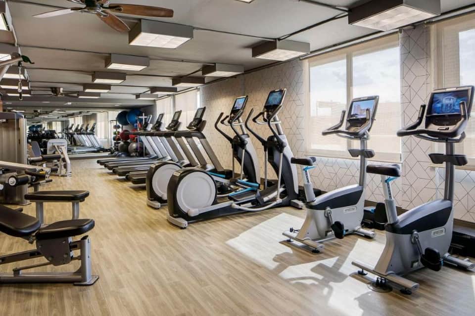 Contemporary fitness center with rows of stationary bikes, elliptical machines, and large windows