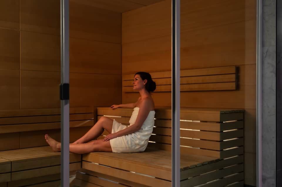 Woman relaxing in modern wooden sauna with horizontal slat paneling and glass doors