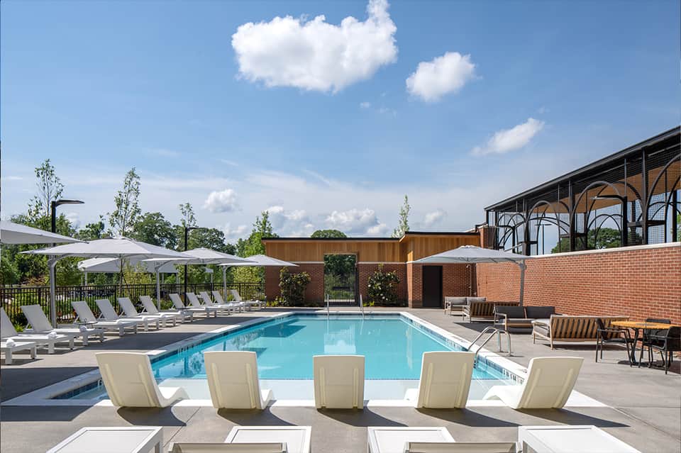 Modern pool surrounded by white umbrellas and gray loungers with brick architecture