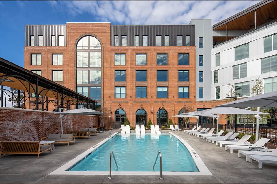 Resort pool courtyard with brick building, white lounge chairs, and umbrellas in contemporary setting