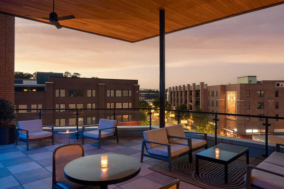 Urban rooftop lounge at dusk with blue chairs, fire pit, and city skyline views