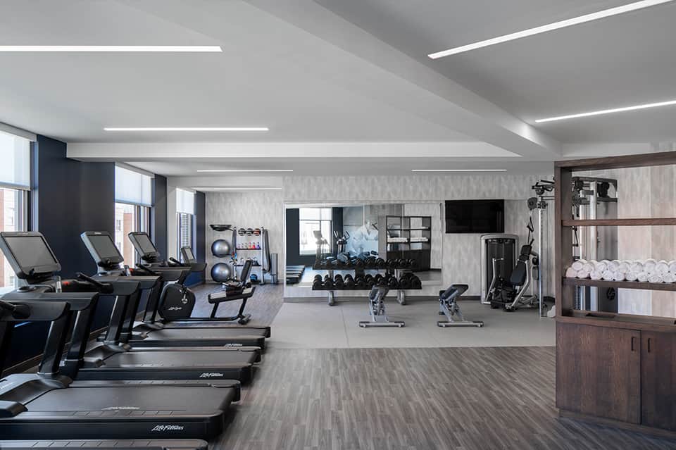 Modern fitness center with treadmills, cardio equipment, weights, and TV screens