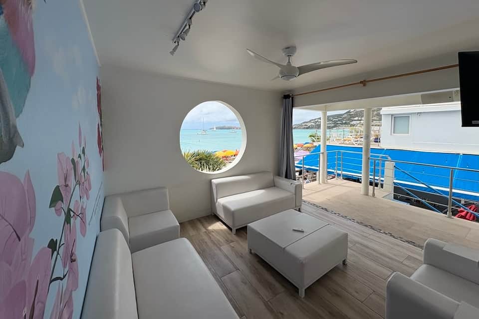 Modern waterfront lounge with white seating, circular porthole window, and ocean views