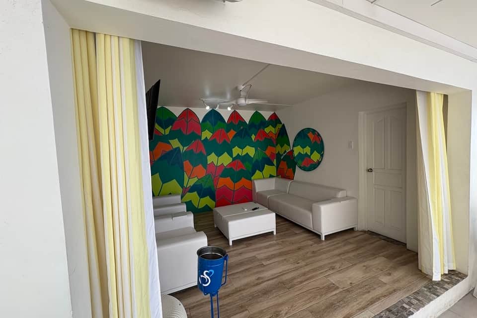 Recreation room with colorful kite-shaped wall art, gray seating, yellow curtains, and wooden flooring